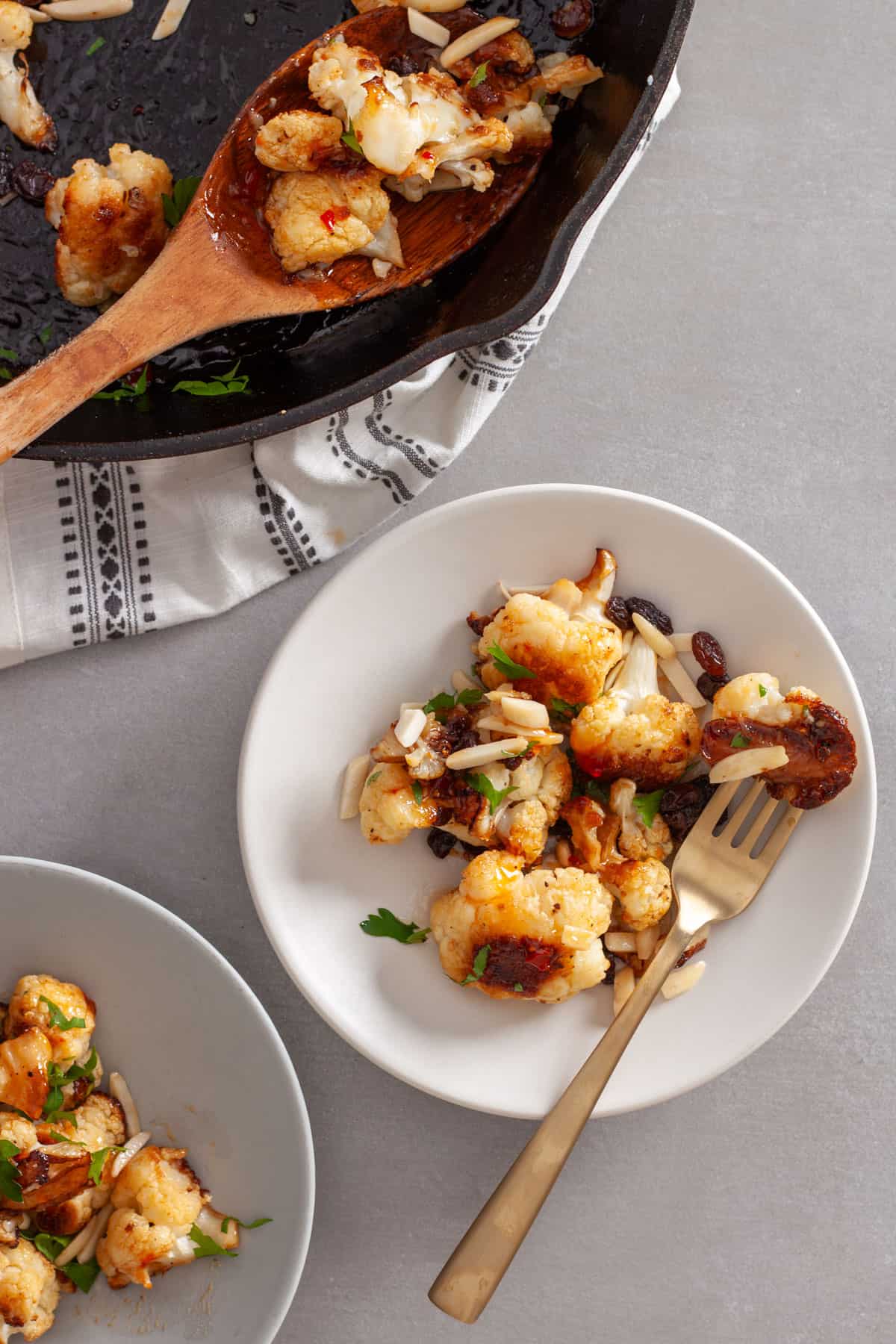 A serving of sweet chili roasted cauliflower on a white plate with a skillet to the side.