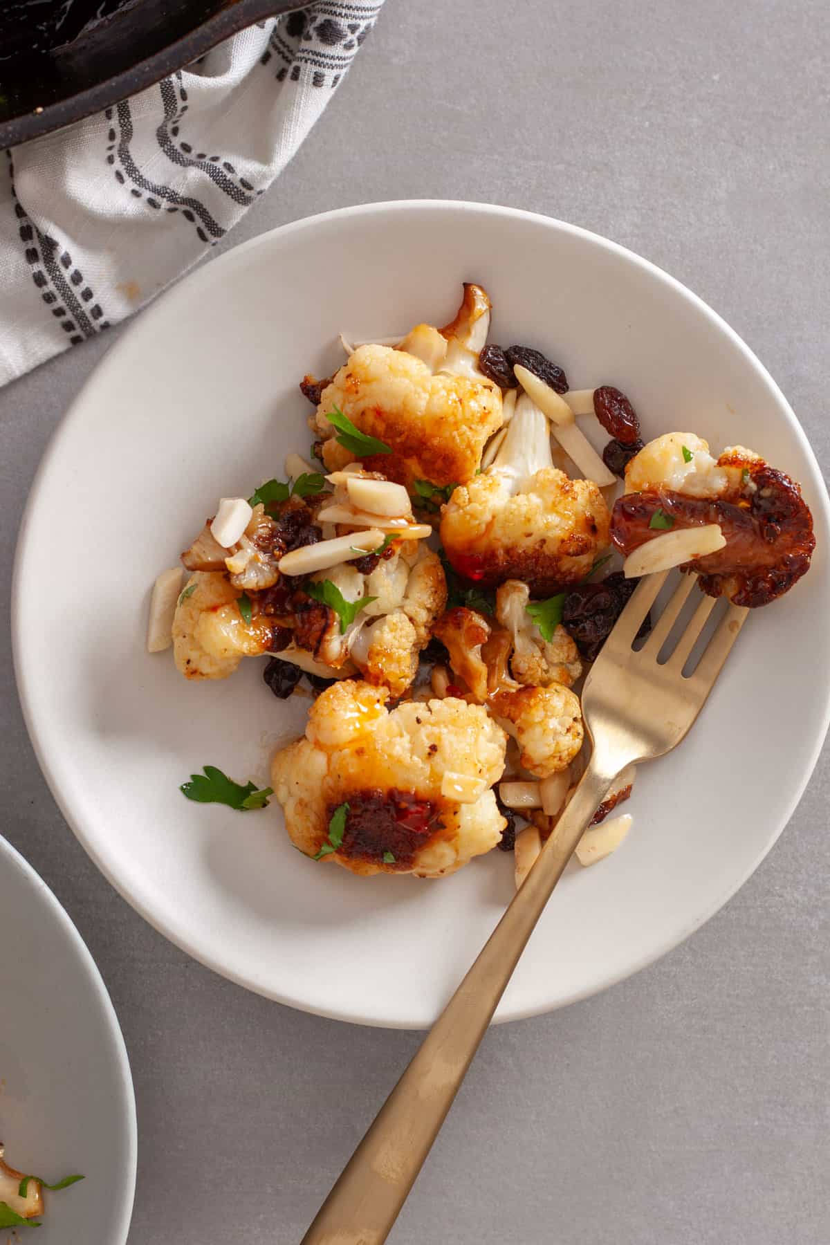A small white plate with sweet chili roasted cauliflower and a fork piercing one cauliflower.