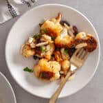 A serving of sweet chili roasted cauliflower on a white plate with a skillet to the side.