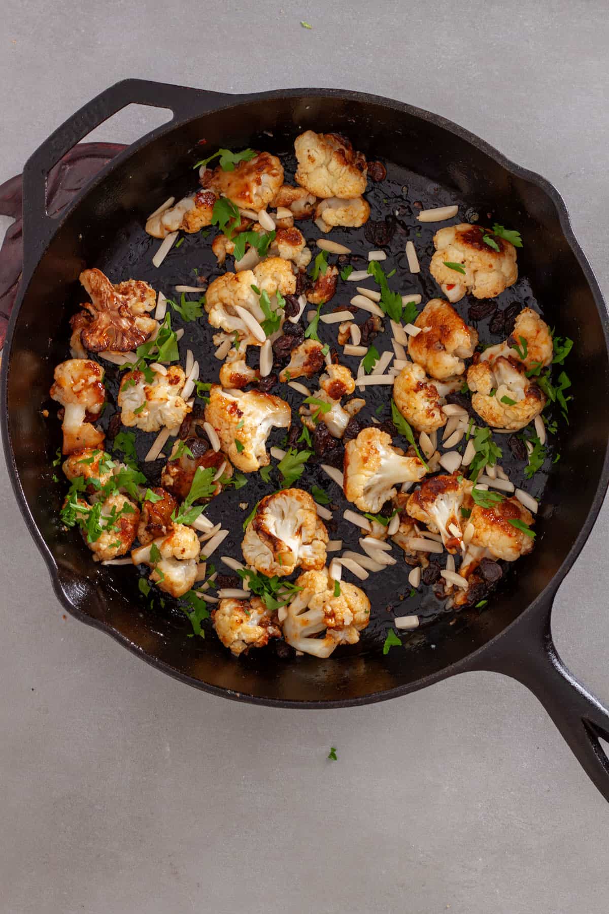 Sweet chili roasted cauliflower in a cast iron skillet topped with fresh parsley, slivered almonds and raisins.