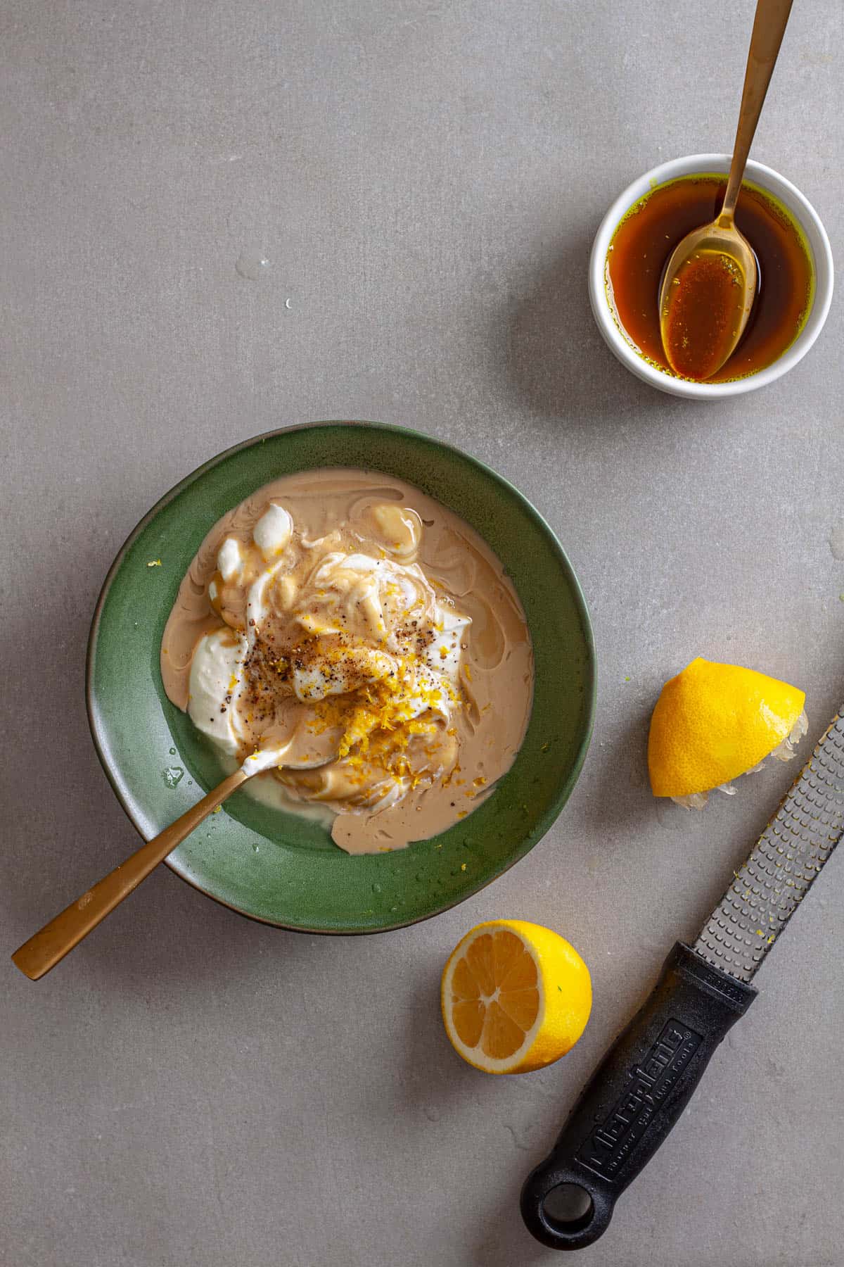 Tahini yogurt sauce getting stirred together in a green bowl with a lemon zested to the side.