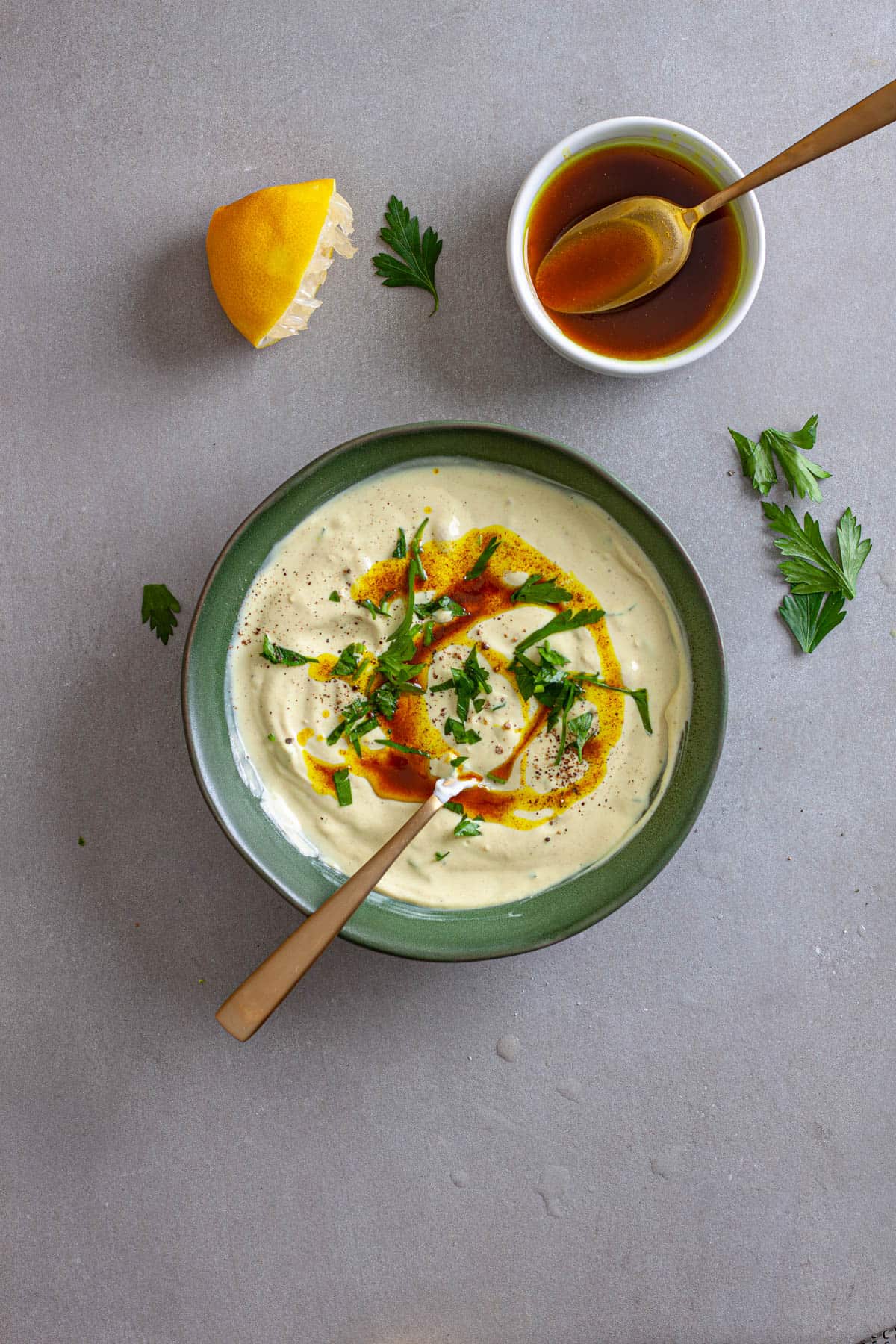 Tahini yogurt sauce in a green bowl topped with chopped parsley and cumin oil.