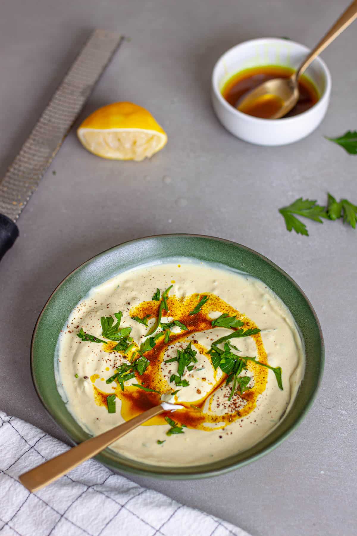A green bowl with tahini yogurt sauce topped with chopped parsley and cumin oil.