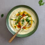 A bowl of tahini yogurt sauce topped with chopped parsley and cumin oil.