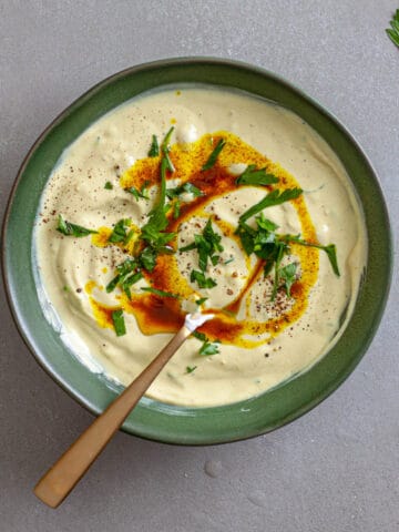 A bowl of tahini yogurt sauce topped with chopped parsley and cumin oil.