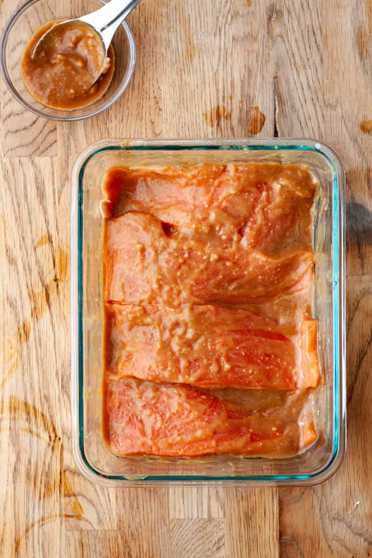 Four portions of salmon in a dish with miso marinade on a butcherblock countertop.