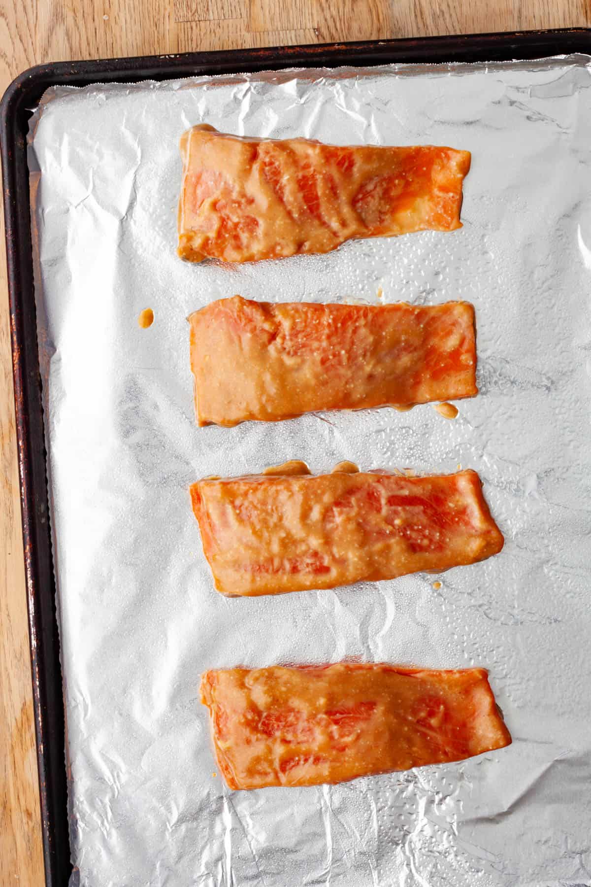 A baking sheet covered in aluminum foil with miso marinated salmon ready to get roasted.