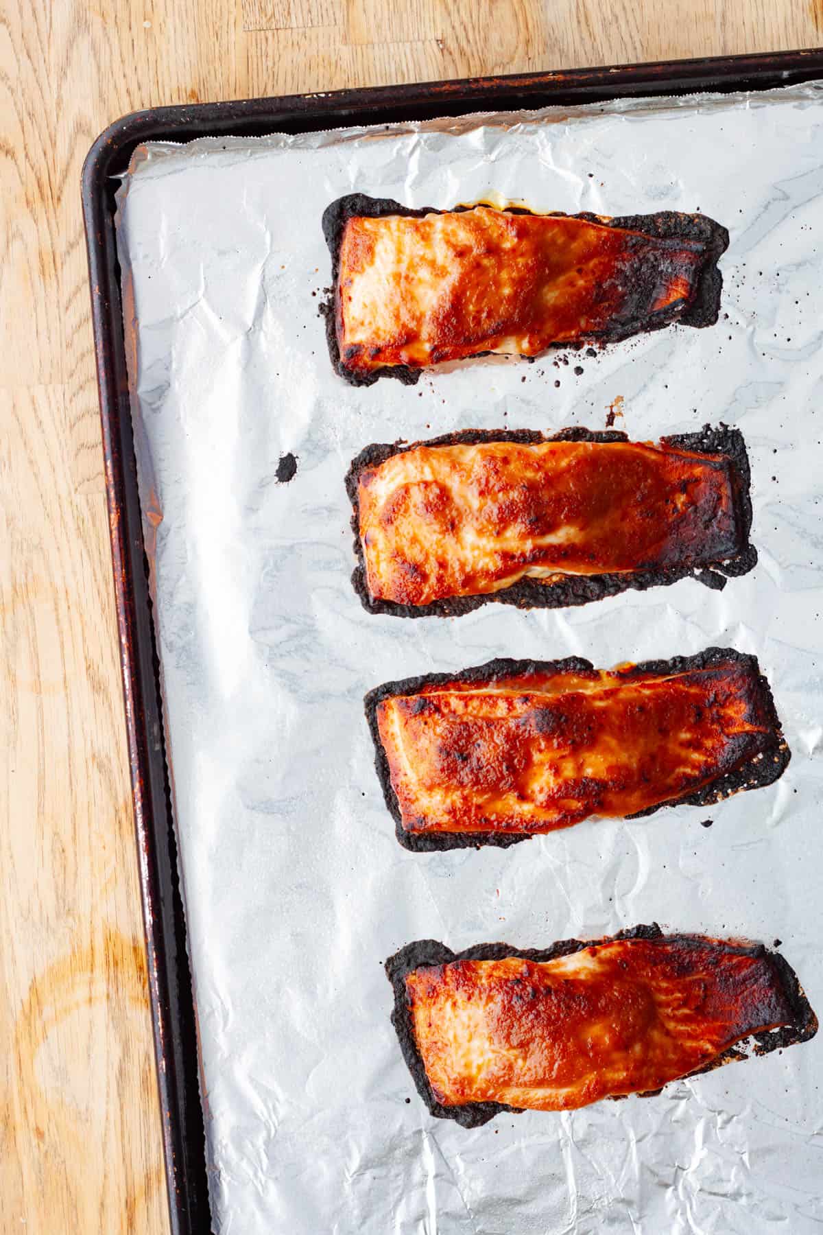 Portions of roasted and broiled miso salmon on a foil lined baking sheet.