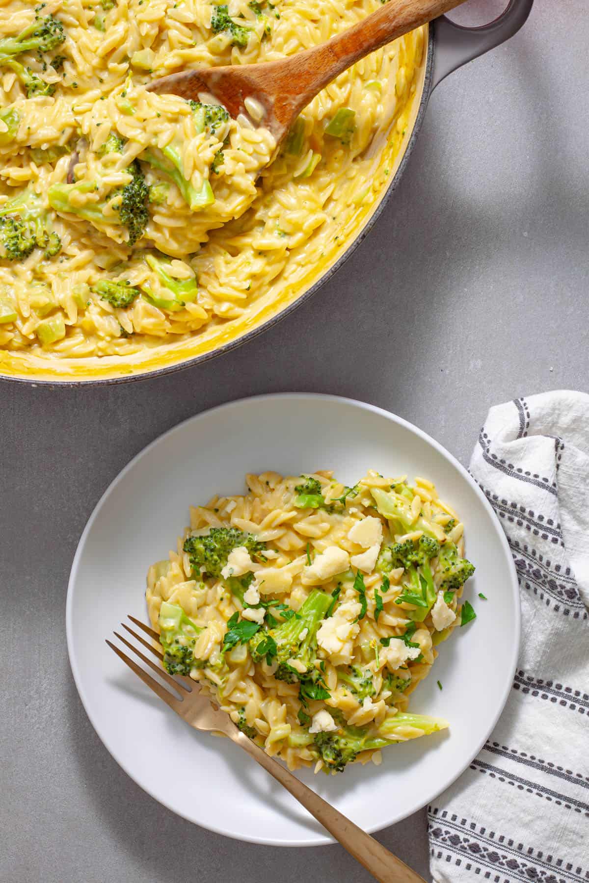 A serving of creamy broccoli orzo on a white plate with a pot of more off to the side.