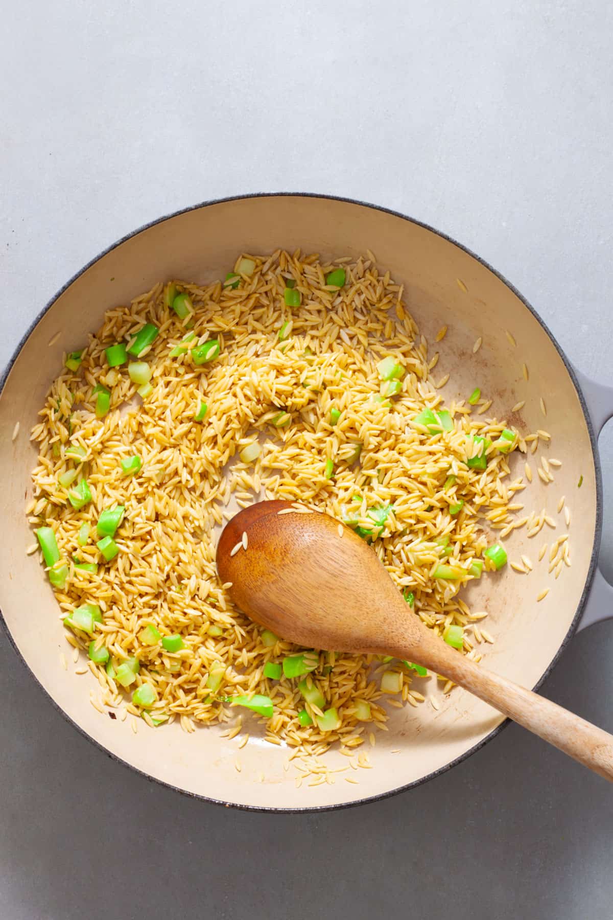 Orzo and chopped broccoli stem in a large skillet cooking in oil.