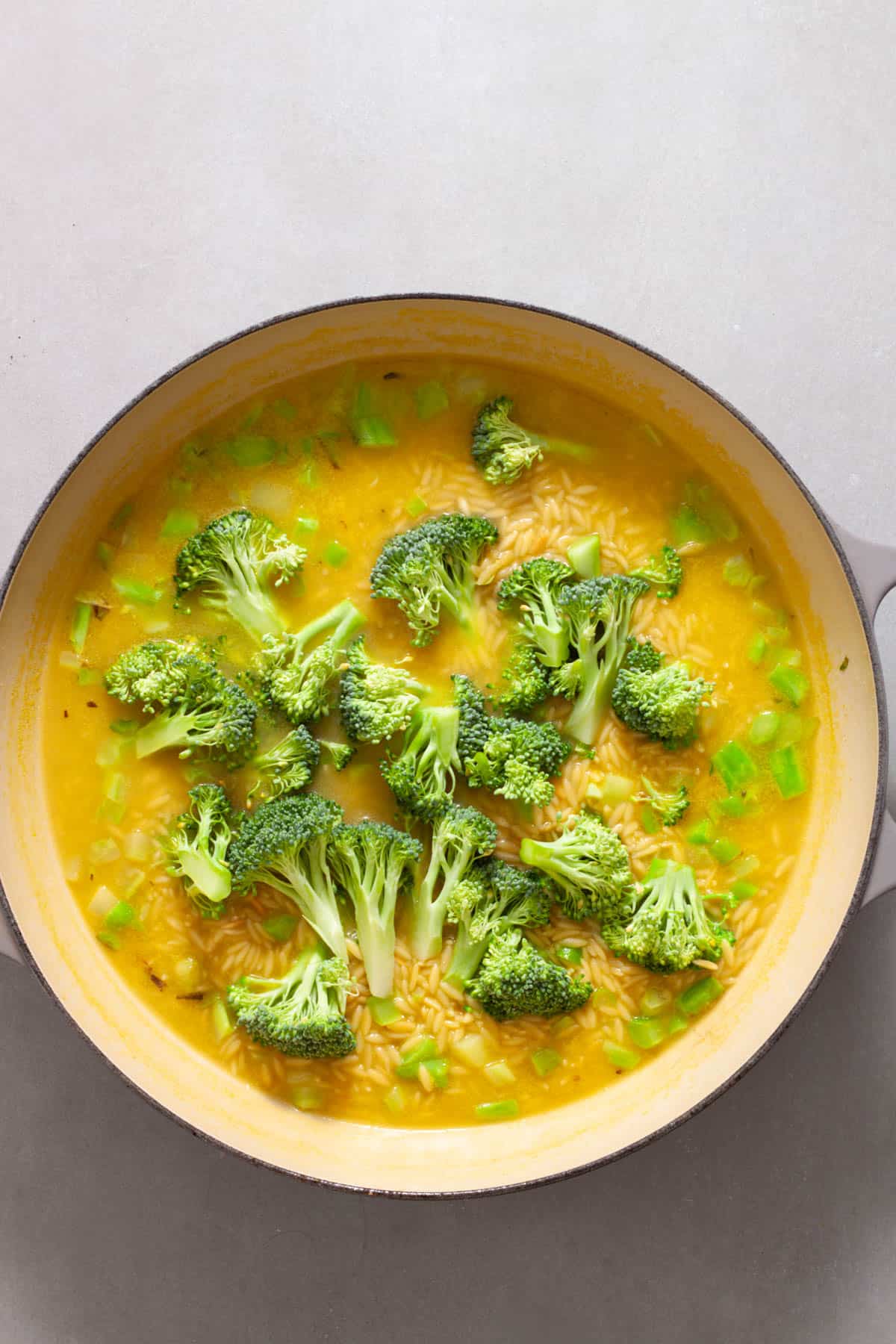 A large skillet with broccoli and orzo cooking in vegetable broth.