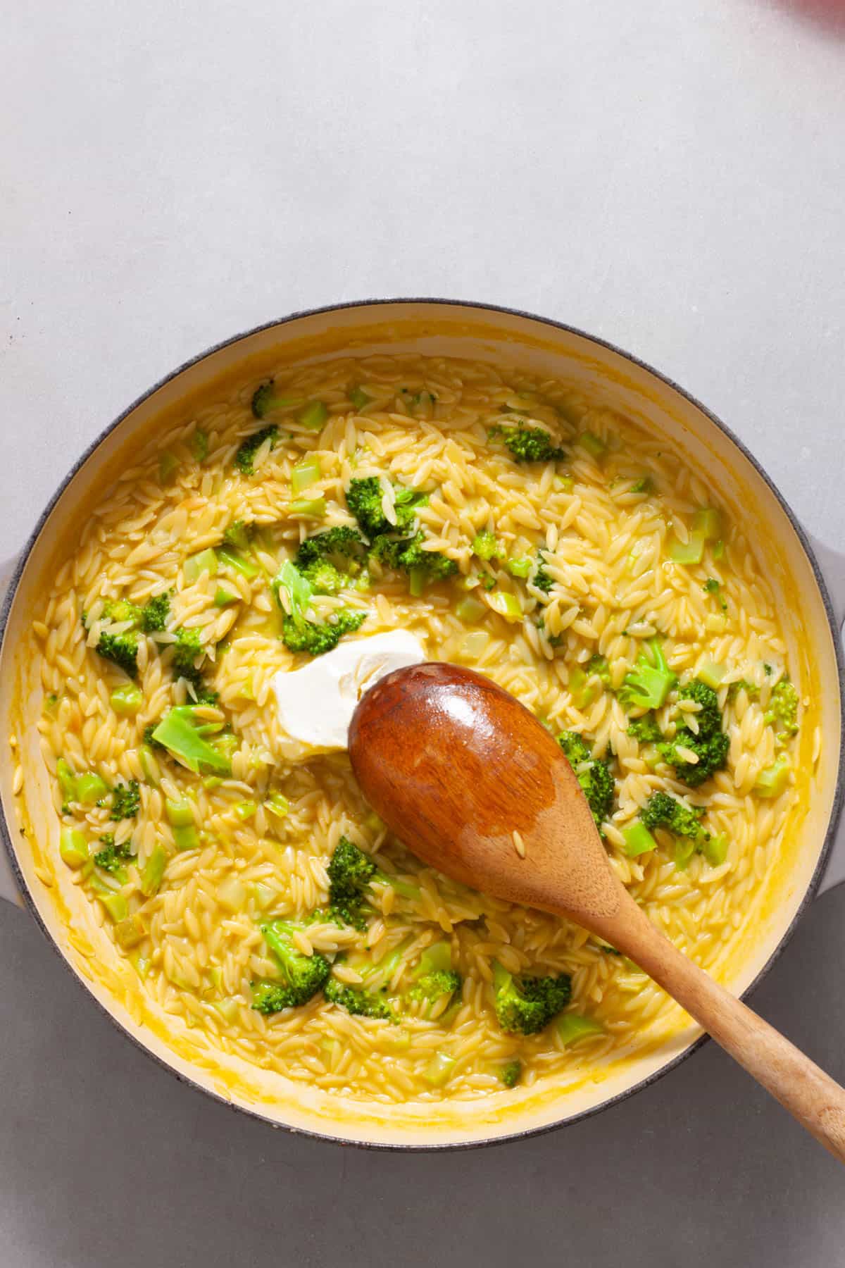 Cream cheese getting stirred into a large skillet with broccoli and orzo.