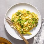A white plate of creamy one-pan broccoli orzo topped with cheese and parsley.