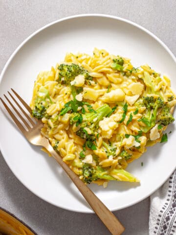 A white plate of creamy one-pan broccoli orzo topped with cheese and parsley.
