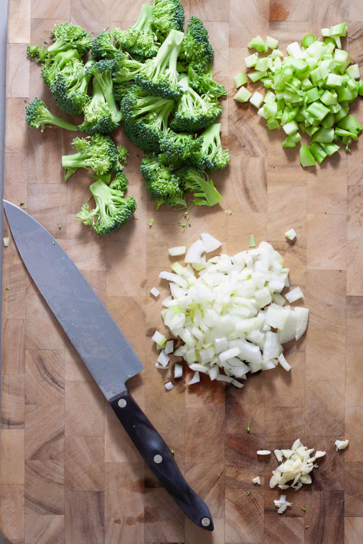 A diced onion and minced garlic on a cutting board with a head of broccoli diced and the florets chopped.