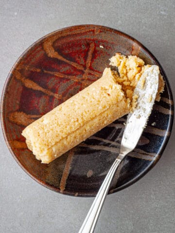A roll of homemade miso butter on a small brown dish with a small butter knife to the side.