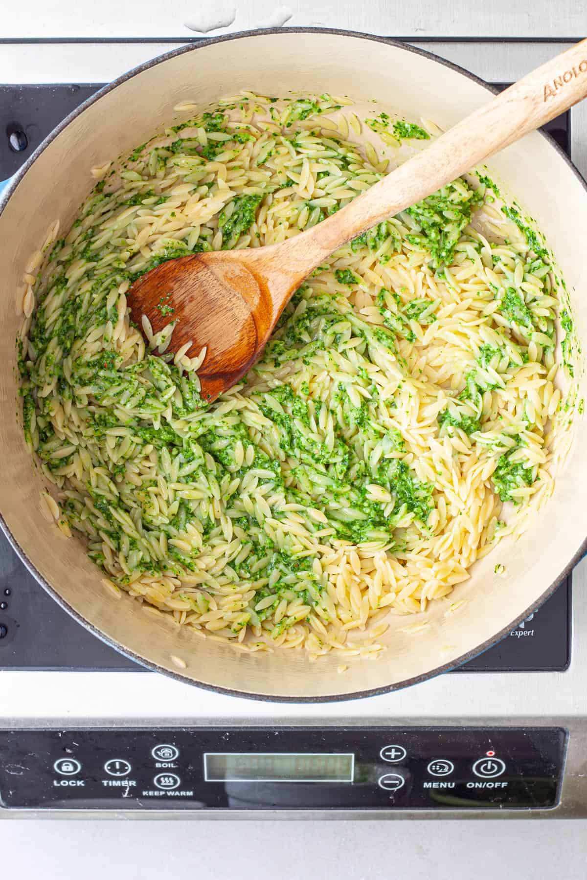 Pesto getting stirred into a large pot of orzo.