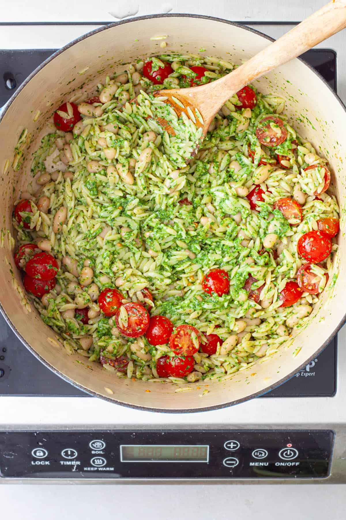 White beans getting stirred into a large pot of orzo with pesto and tomatoes.
