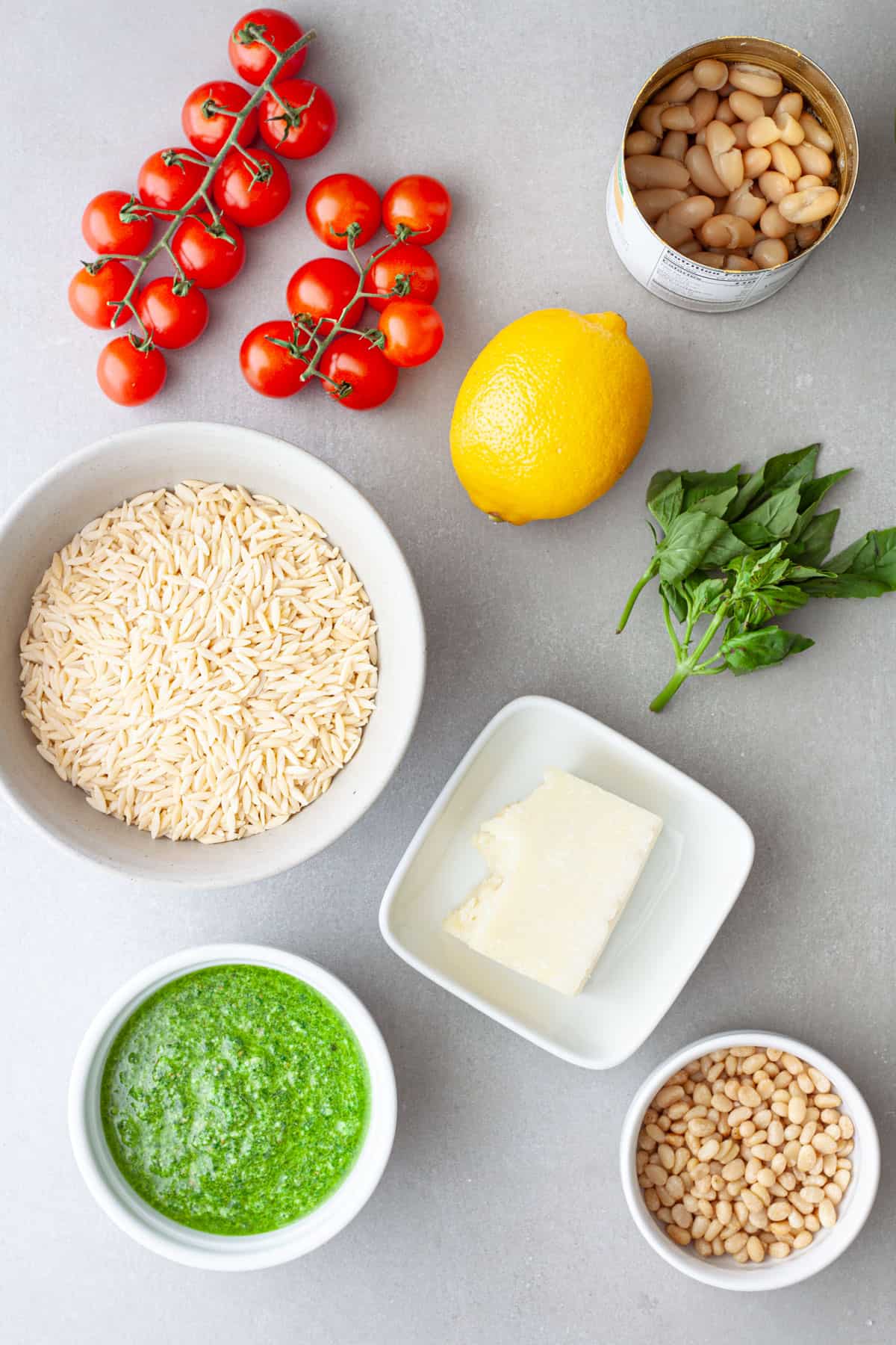 Ingredients for pesto orzo salad on a gray table.