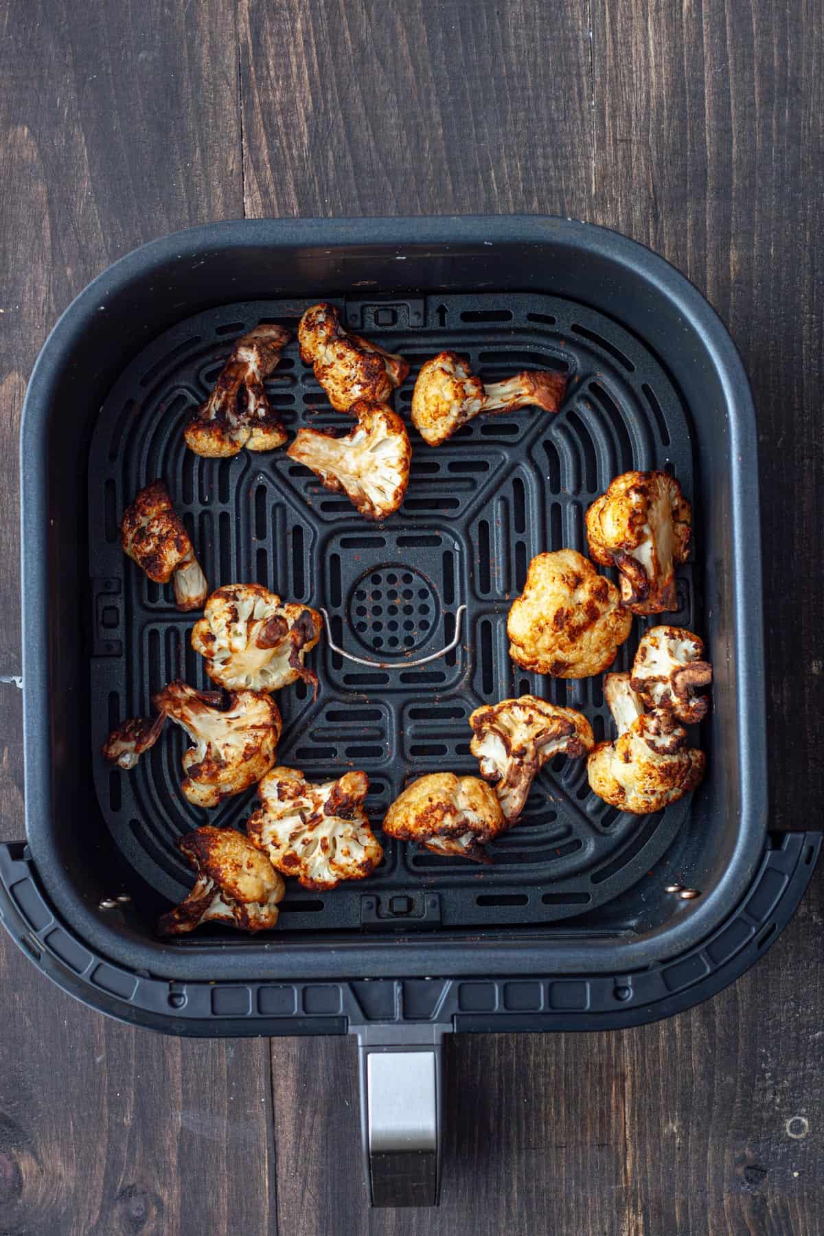 An air fryer basket with golden brown roasted miso cauliflower.