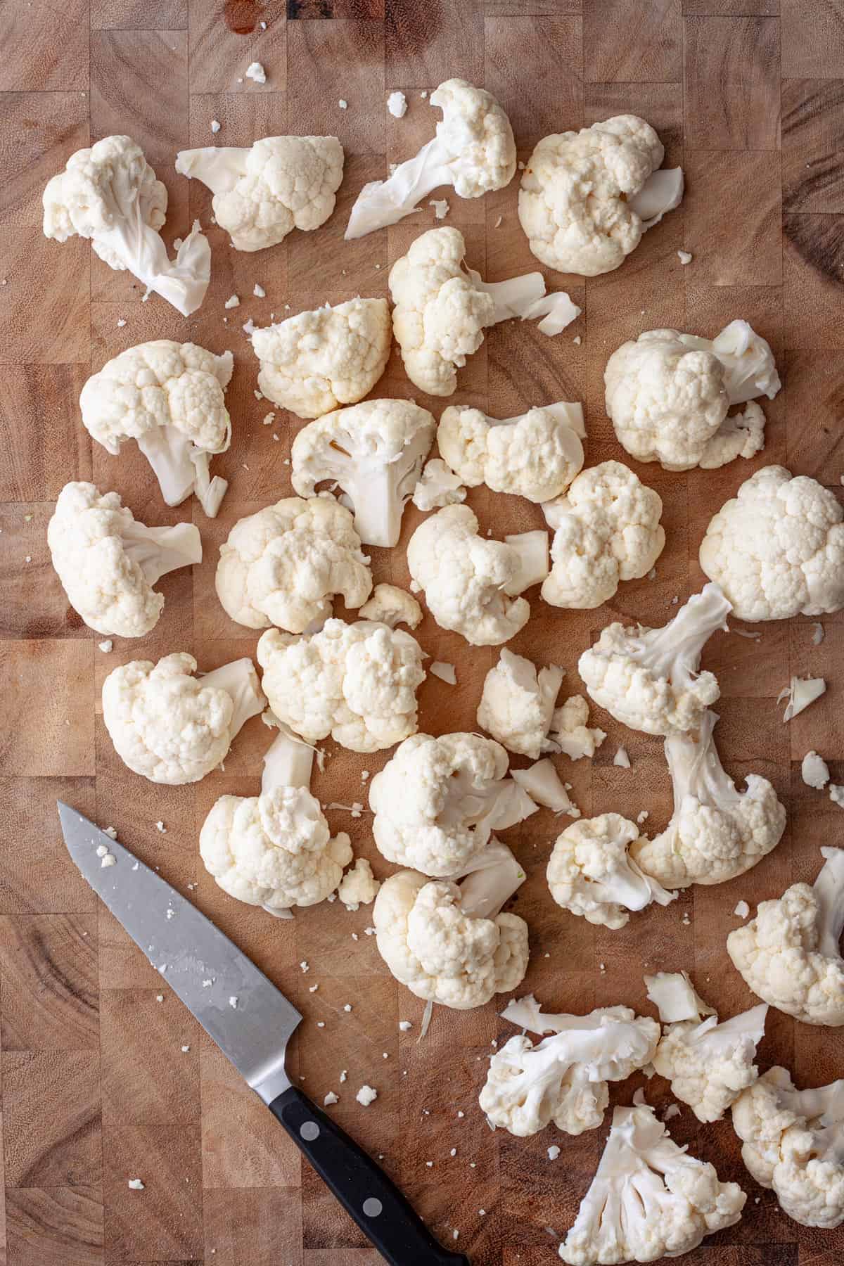 Cauliflower florets cut into bite-sized pieces on a butcher block cutting board.
