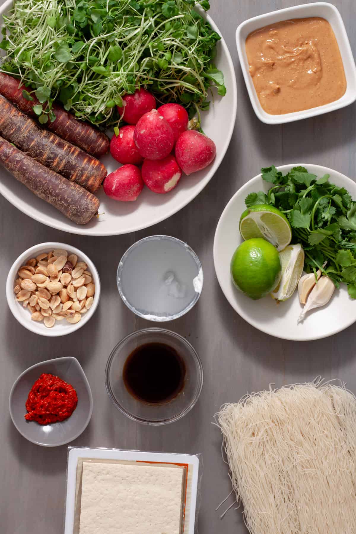 Ingredients for summer roll bowls with crispy tofu and peanut sauce on a gray table.