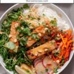 A white bowl with a summer roll salad topped with crispy peanut tofu, herbs, peanuts and peanut sauce.