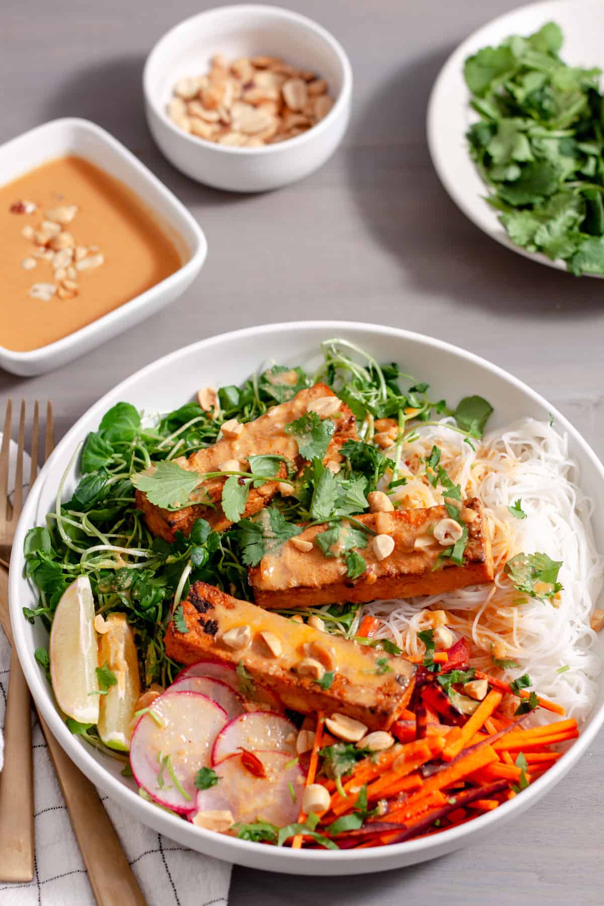 A white bowl with a summer roll salad topped with crispy peanut tofu, herbs, peanuts and peanut sauce.