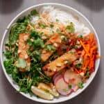 A white bowl with a summer roll salad topped with crispy peanut tofu, herbs, peanuts and peanut sauce.