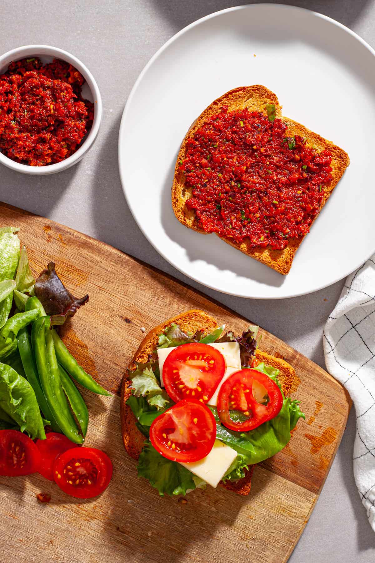 A sandwich with vegetables, cheese and homemade sun-dried tomatoes getting assembled on a cutting board.