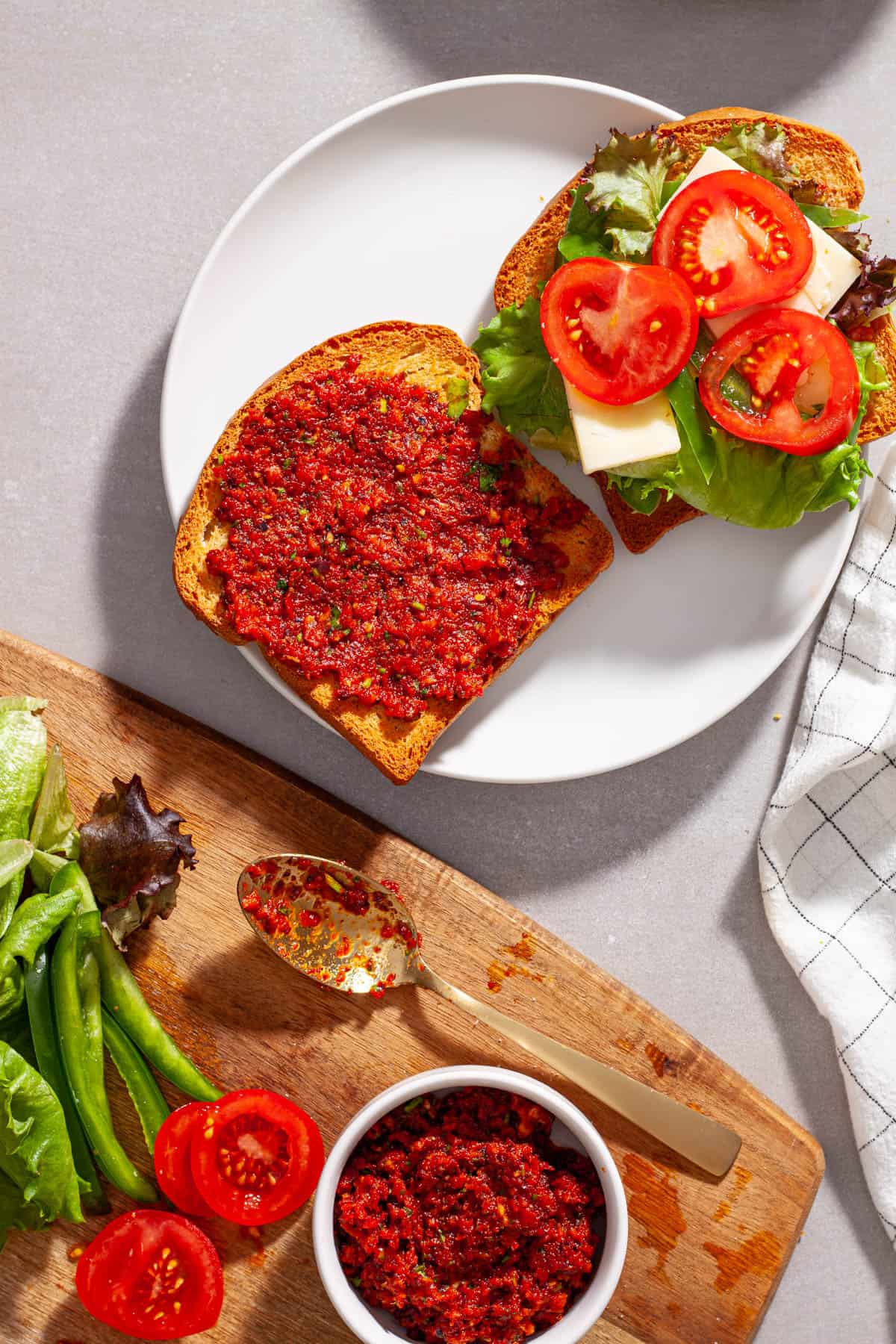 A plate with a sandwich made with homemade sun-dried tomato spread, with lettuce, tomato, peppers and cheese.