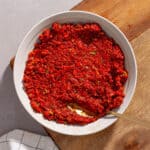 A close-up shot of sun-dried tomato spread in a small bowl on a cutting board.