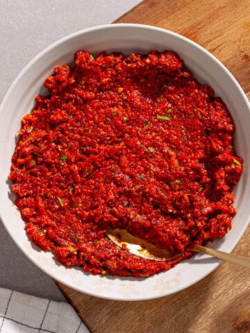 A close-up shot of sun-dried tomato spread in a small bowl on a cutting board.