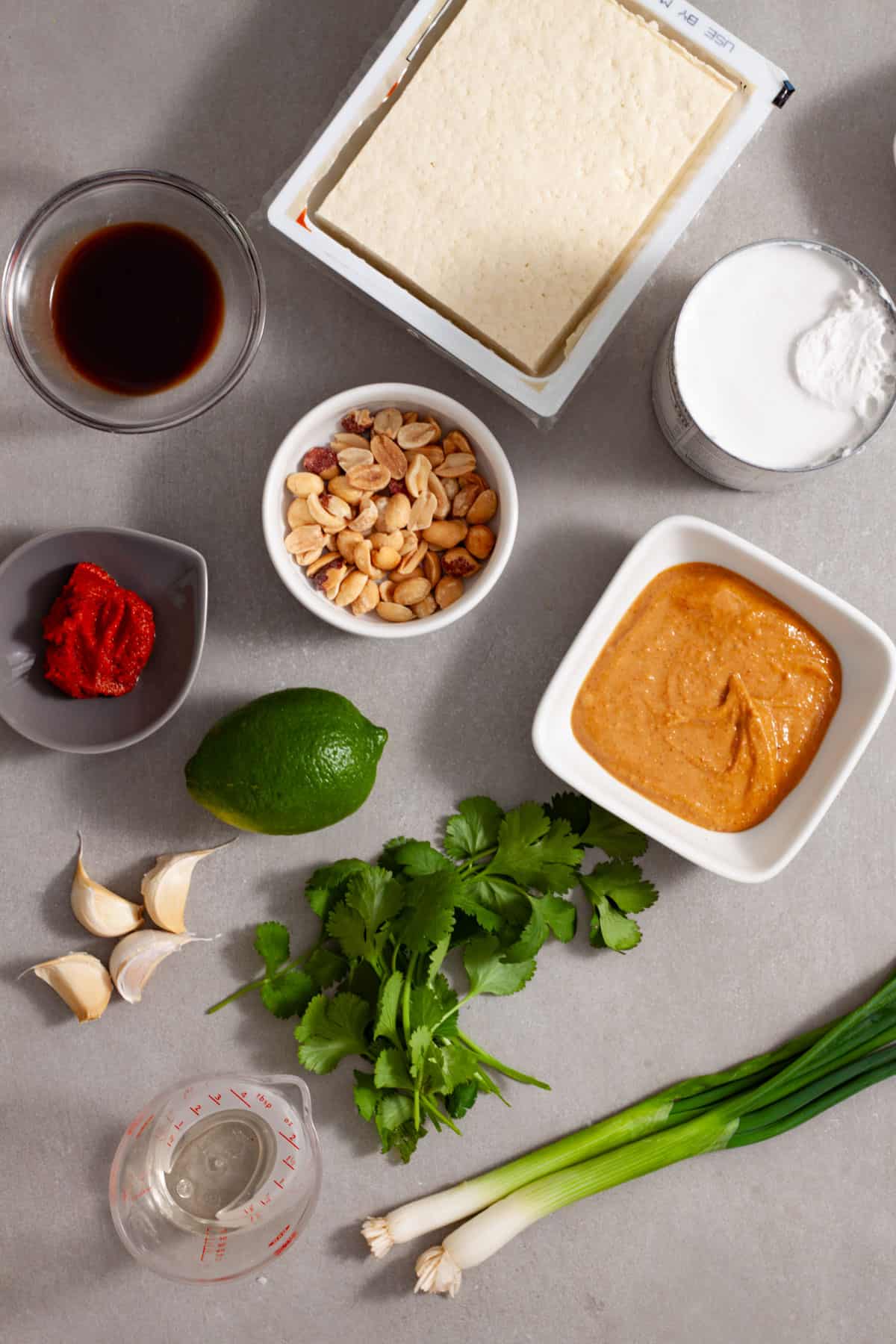 Ingredients for tofu satay on a gray table in small white bowls.