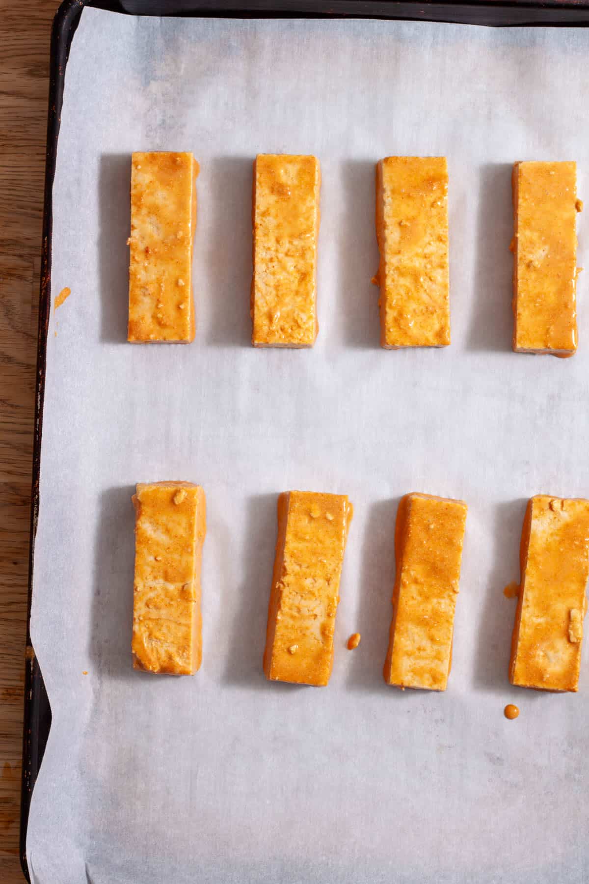 Strips of marinated extra firm tofu on a parchment-lined baking sheet.