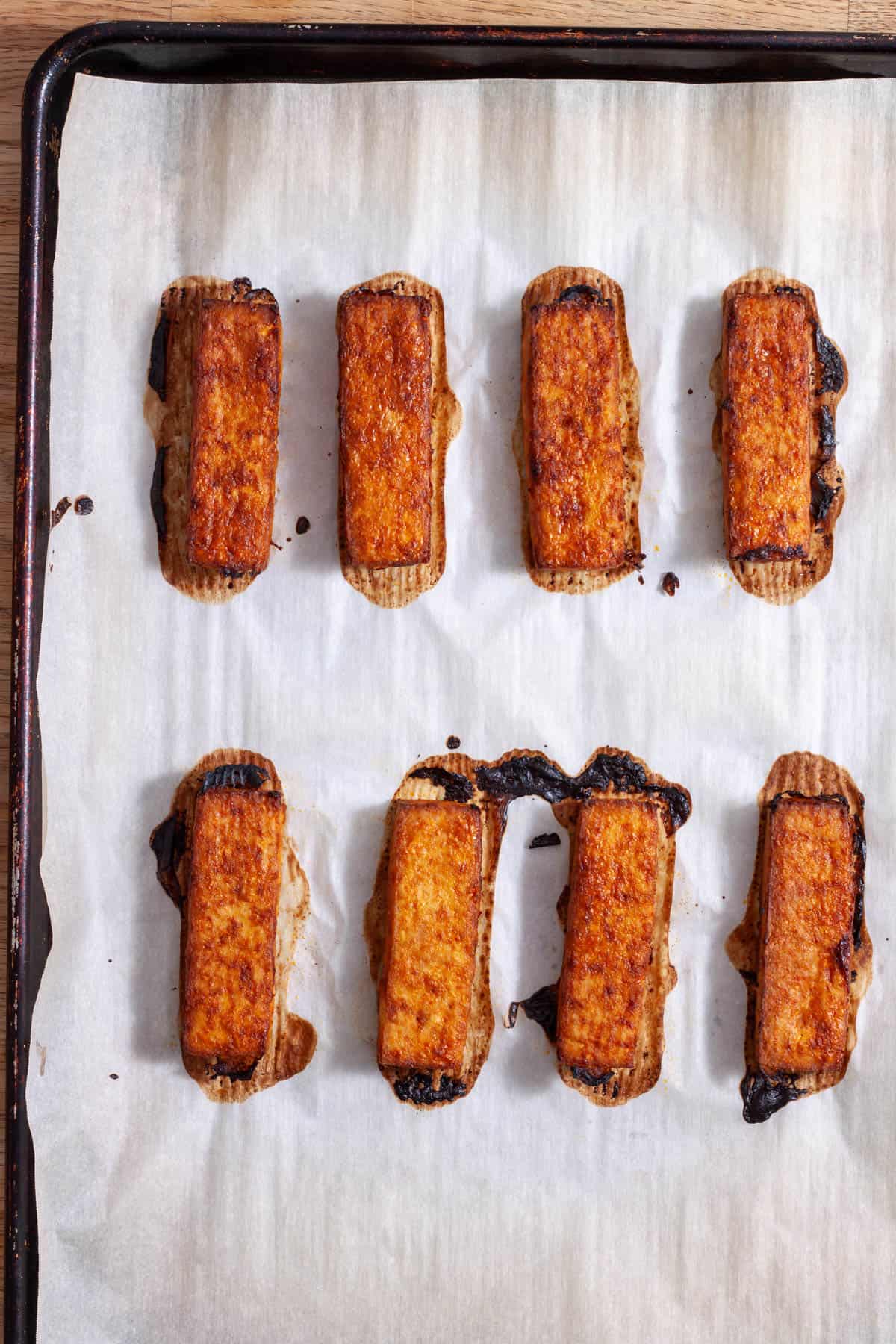 Tofu satay strips fresh out of the oven on a parchment-lined baking sheet.
