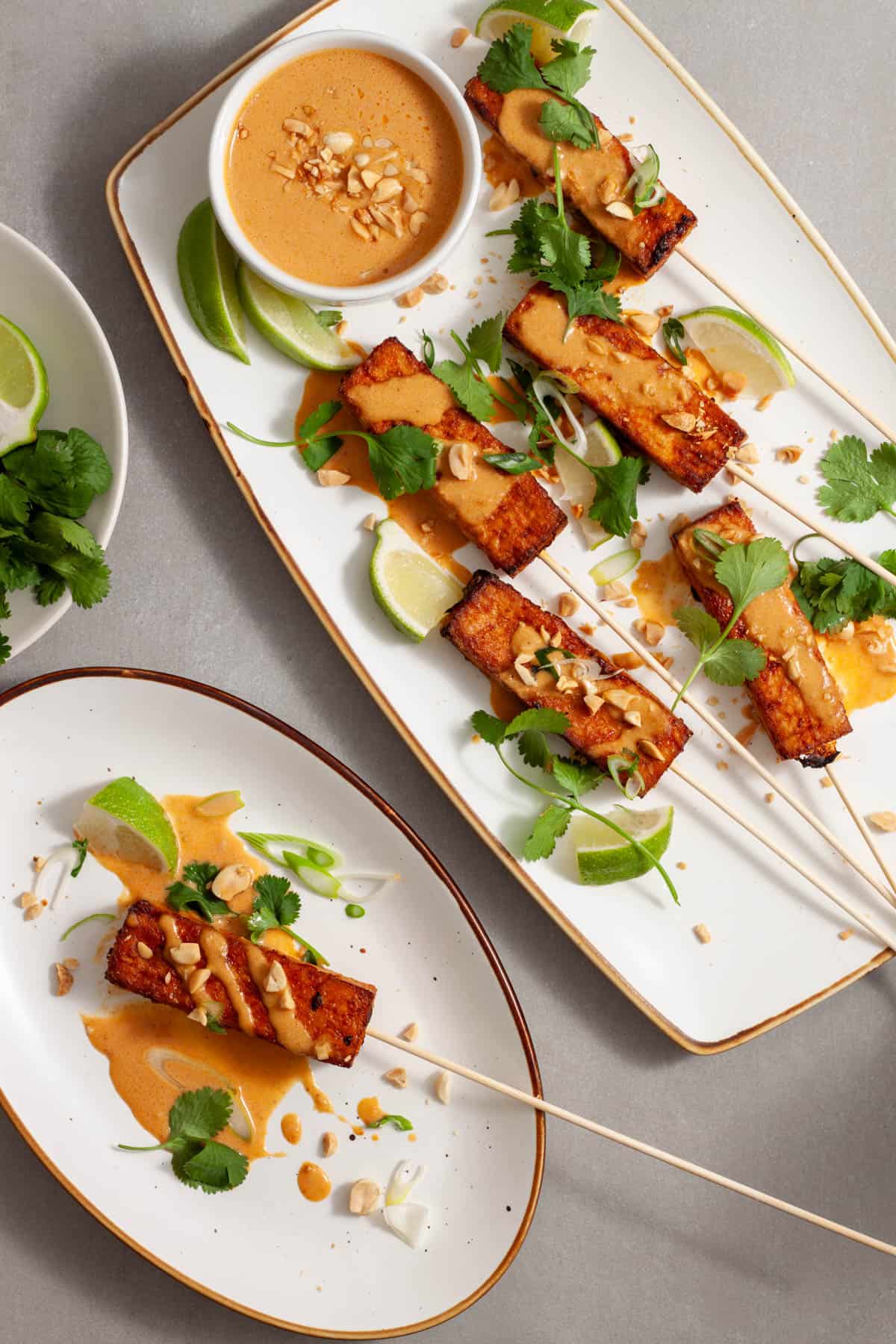 A platter and small plate with tofu satay topped with herbs, peanut sauce and chopped peanuts.