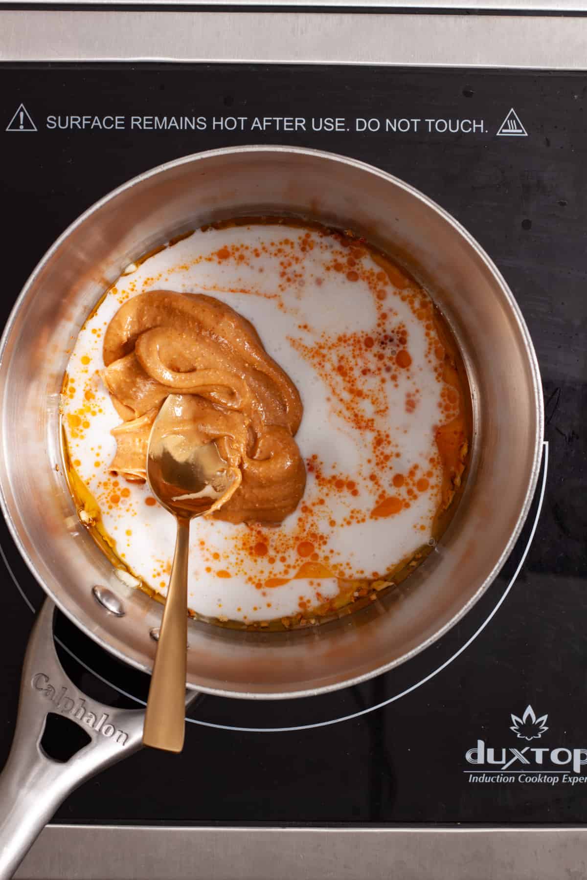 Peanut butter, coconut milk and red chili paste in a small saucepan getting stirred together.