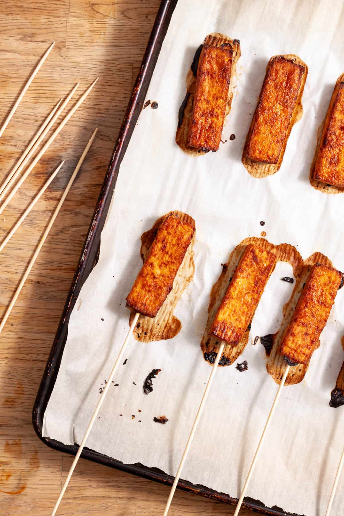 Skewers pressed into strips of tofu satay on a parchment-lined baking sheet.