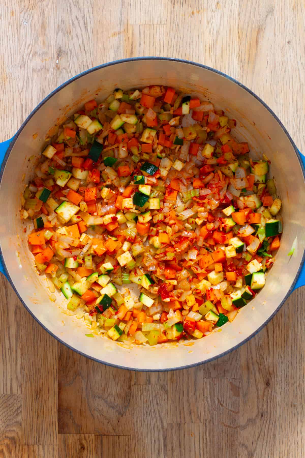 The base of a orzo vegetable soup, including vegetables, tomato paste and garlic, in a blue Dutch oven.