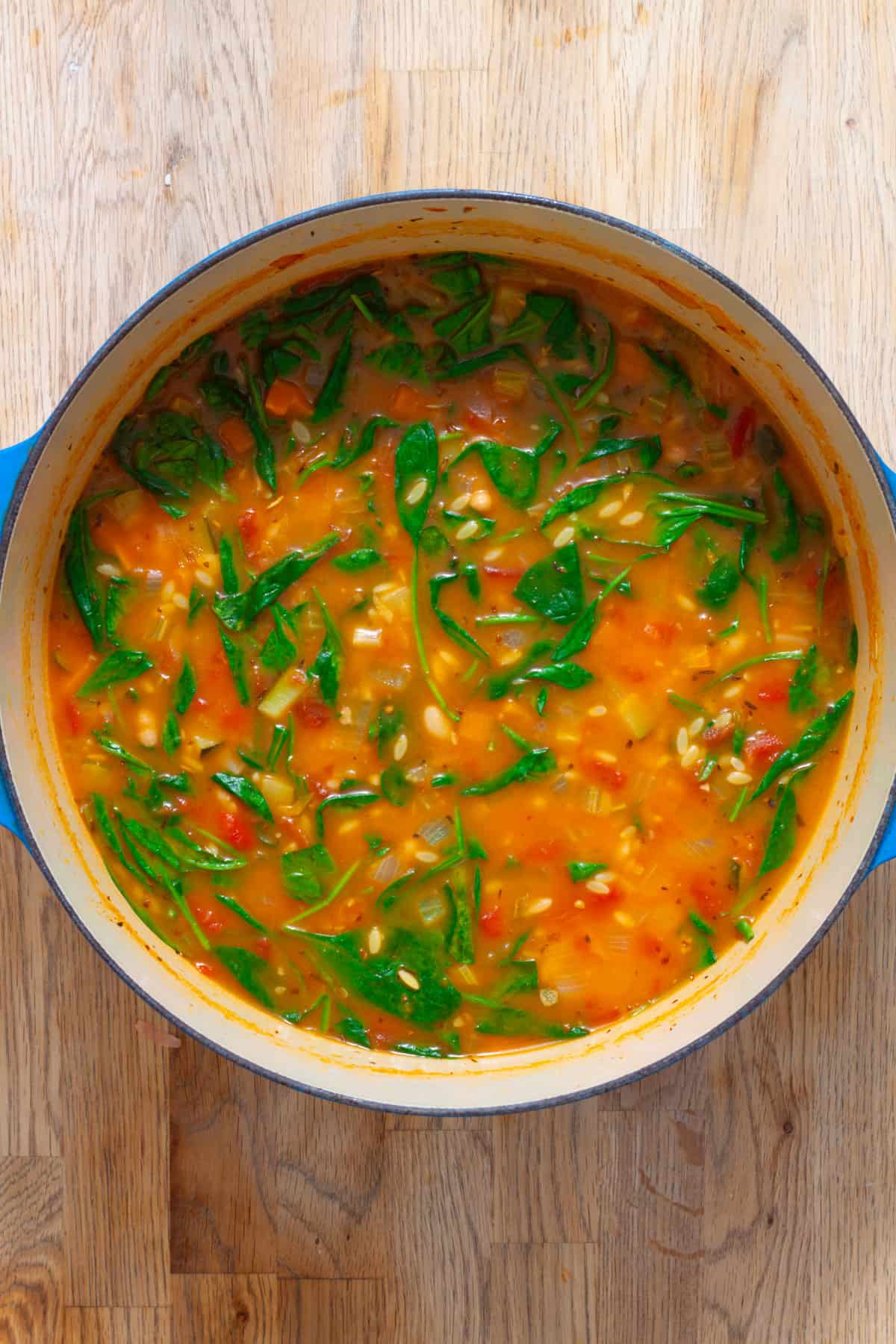 A blue Dutch oven with orzo vegetable soup with spinach and other vegetables.