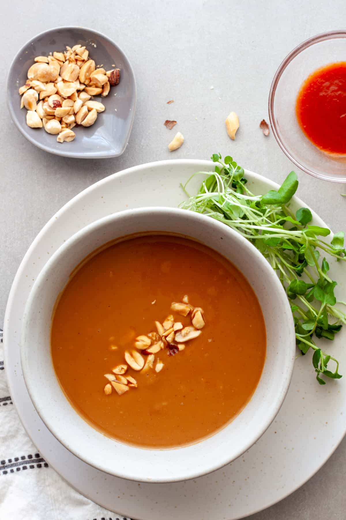 A bowl of Vietnamese peanut sauce in a bowl with greens, peanuts and sriracha to the side.