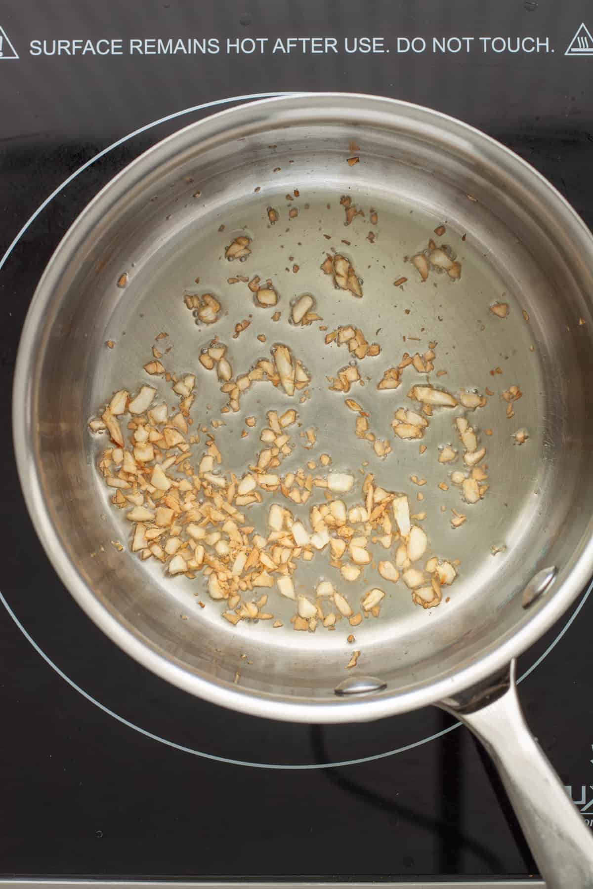 Minced garlic simmering in a small saucepan.