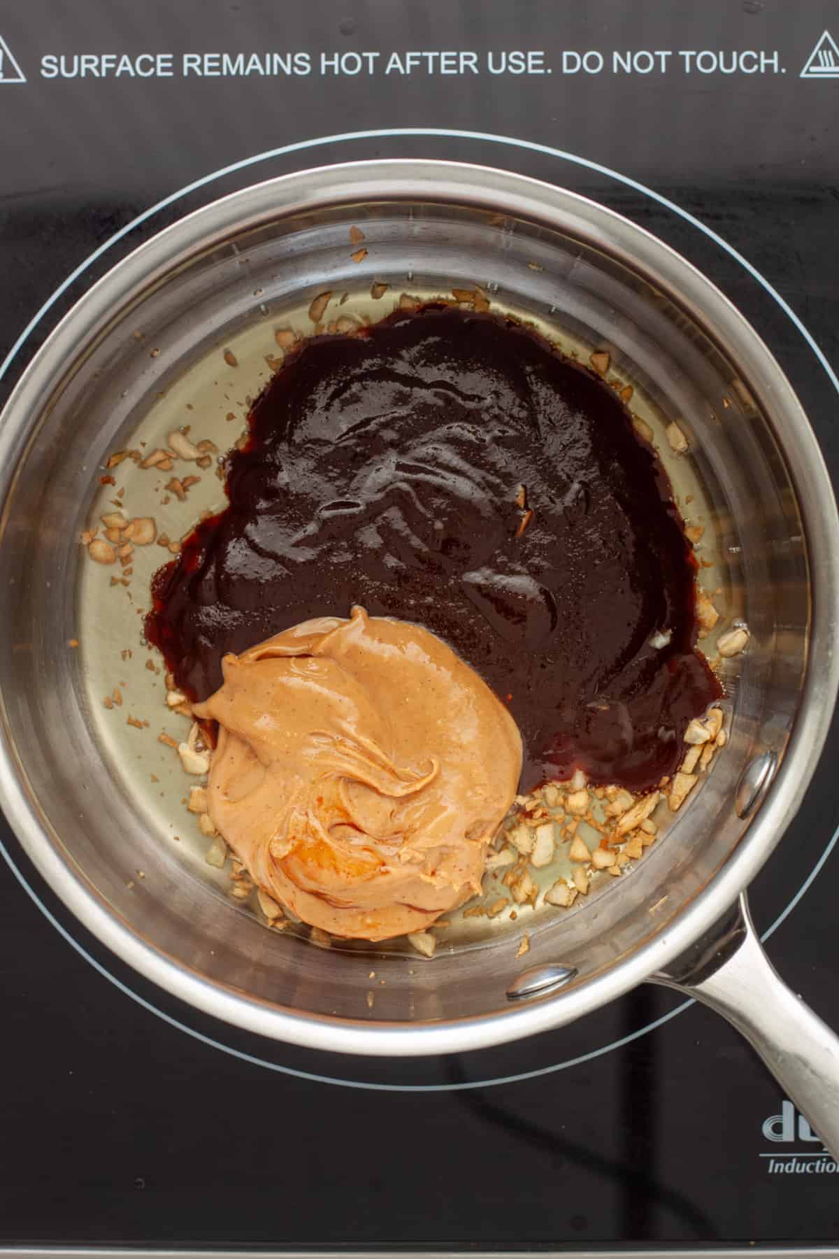 Minced garlic in a small saucepan with hoisin and peanut butter added.