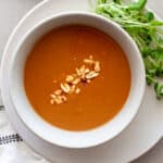 A bowl of Vietnamese peanut sauce in a bowl with greens, peanuts and sriracha to the side.