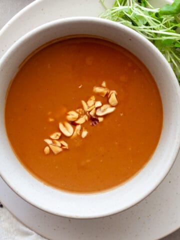 A bowl of Vietnamese peanut sauce in a bowl with greens, peanuts and sriracha to the side.