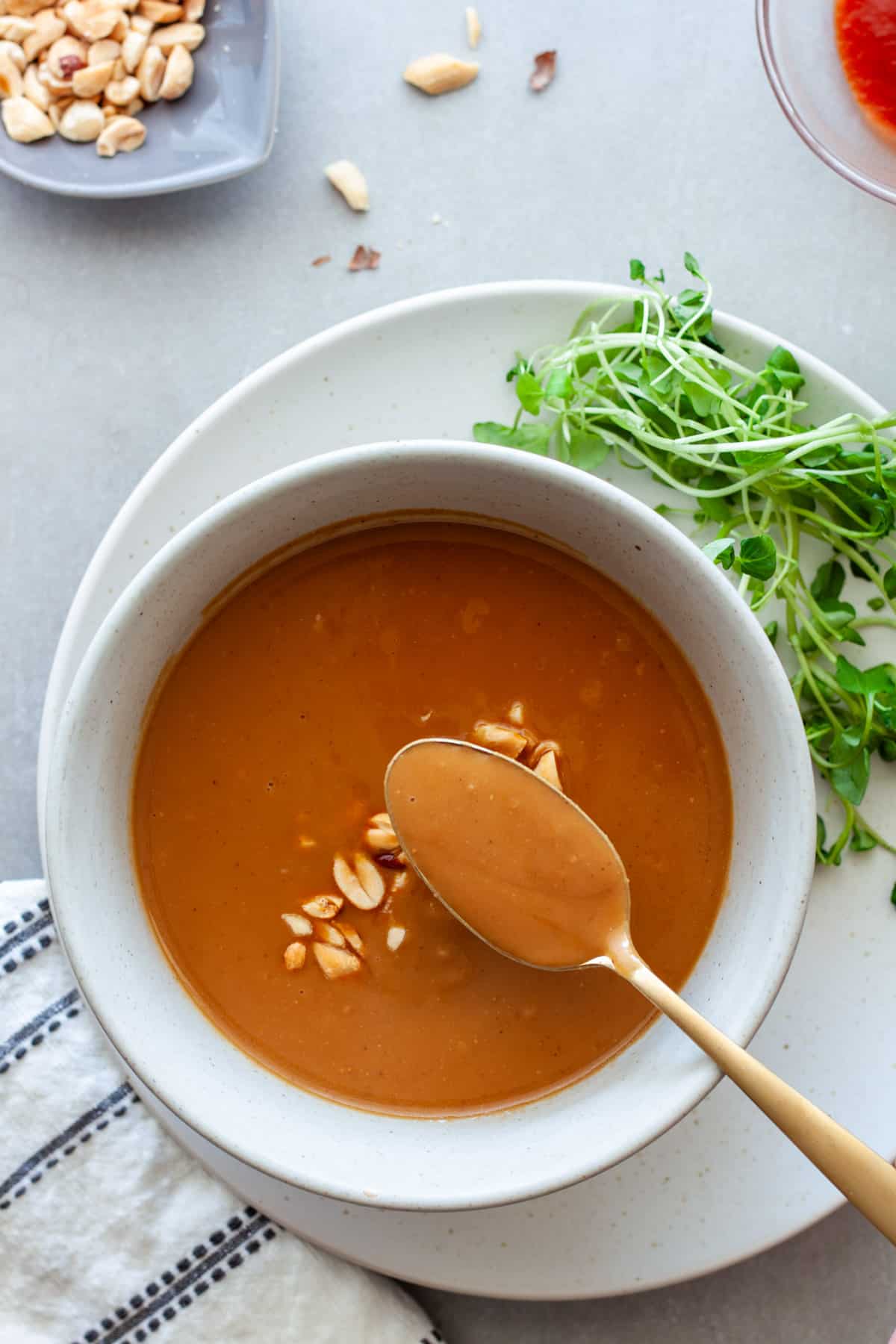 A spoonful of Vietnamese peanut sauce above a bowl of sauce in a small bowl.