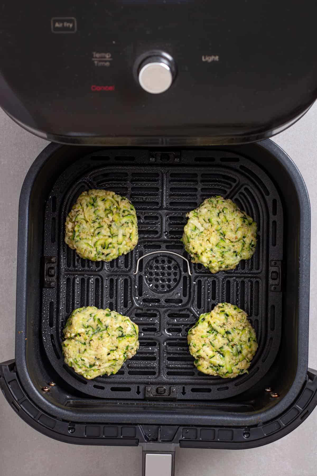 Zucchini patties in a basket of an air fryer ready to get cooked.