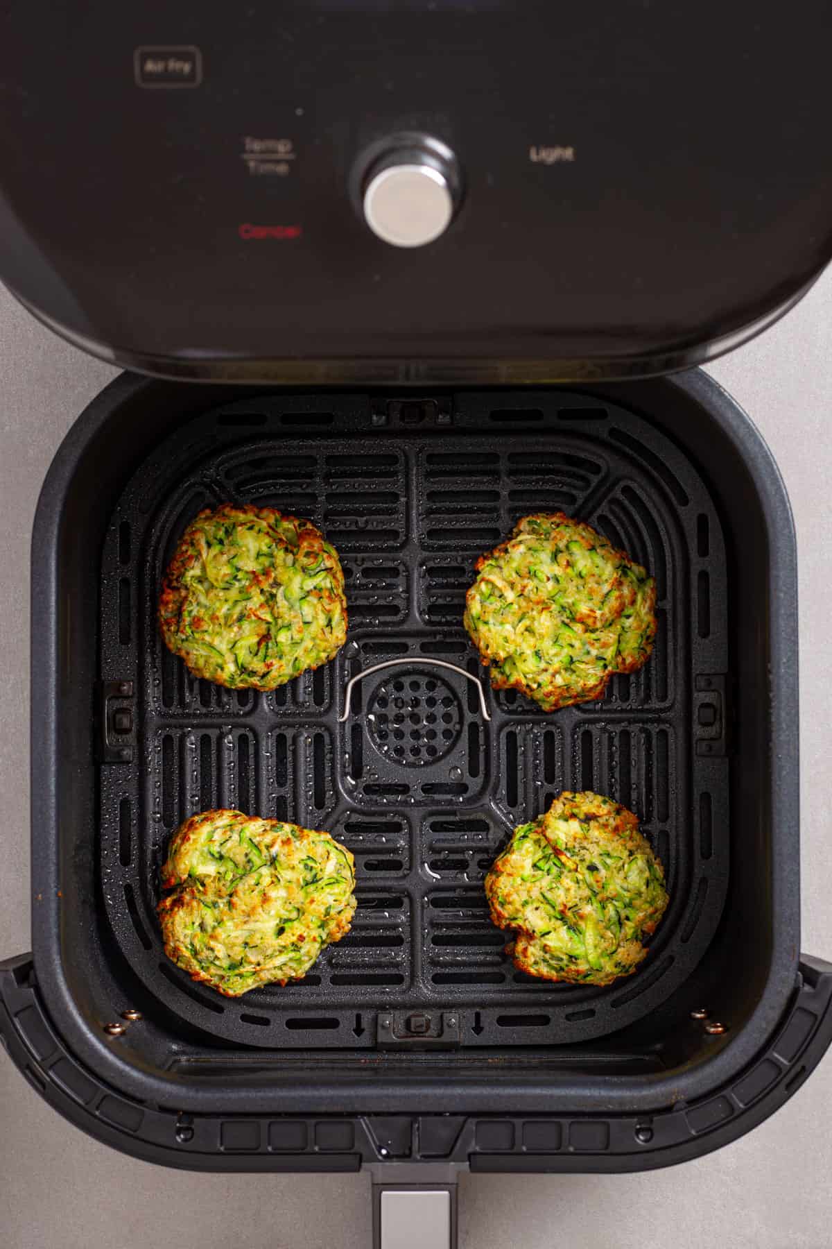 Zucchini fritters in an air fryer halfway cooked.