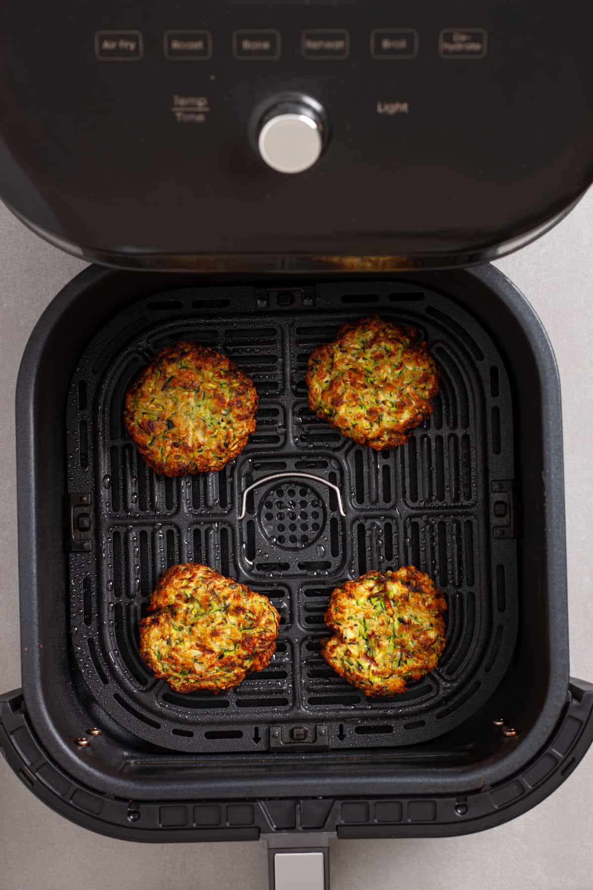 Golden brown air fried zucchini fritters in a basket of an air fryer.